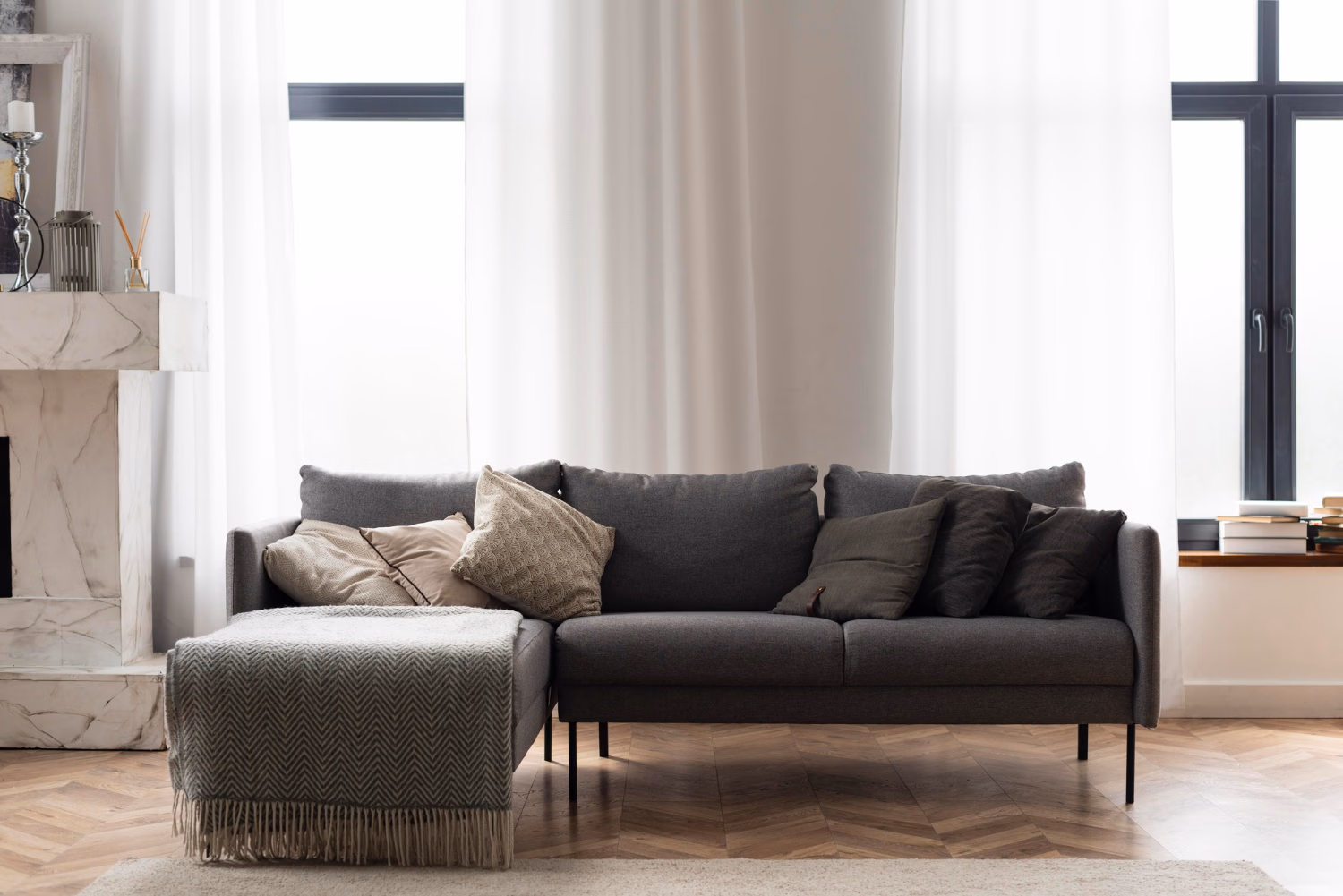 Sofa abu gelap berkaki hitam dengan bantal bertekstur dan ottoman di ruang tamu modern bergaya skandinavia