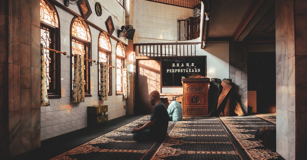 Tranquil scene of two men in peaceful reflection within a sunlit mosque interior, showcasing cultural architecture.