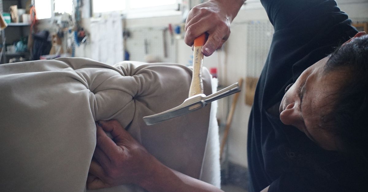 Skilled artisan working meticulously on a sofa using upholstery tools in a workshop.